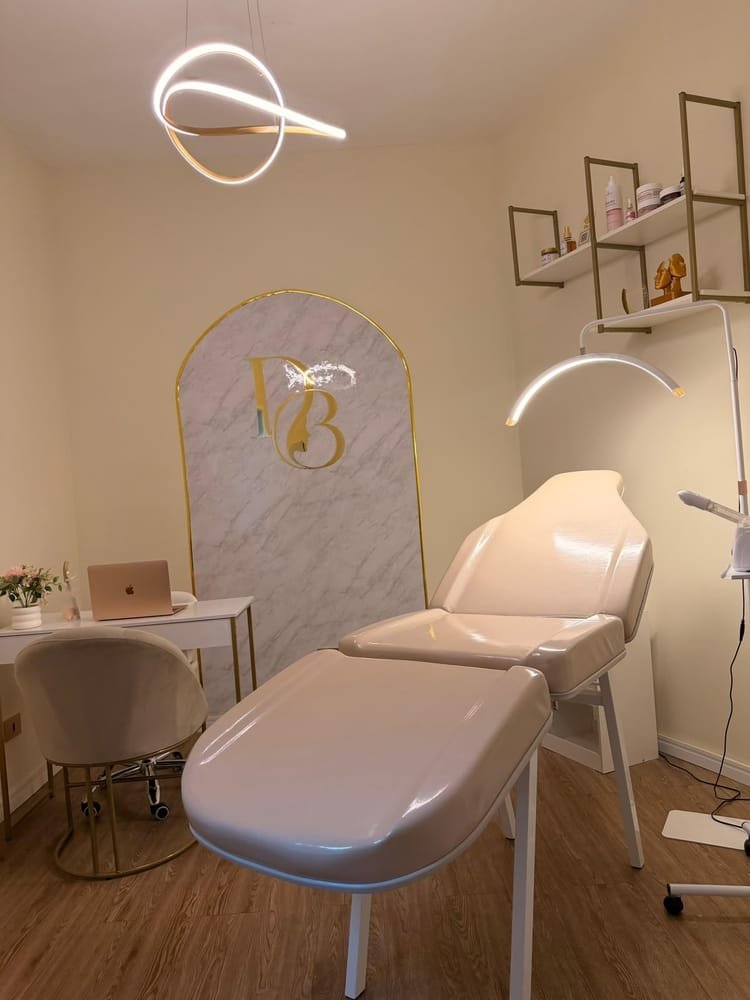 Cabine de atendimento da Daniele Beauty Clinic com maca profissional, luminária e painel de mármore com a marca DB