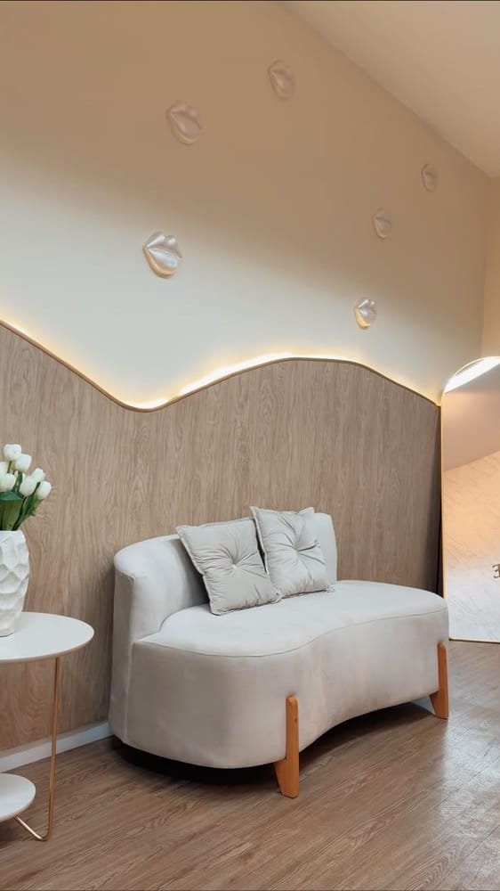 Recepção da clínica com sofá curvo, parede de madeira iluminada e vaso de tulipas brancas