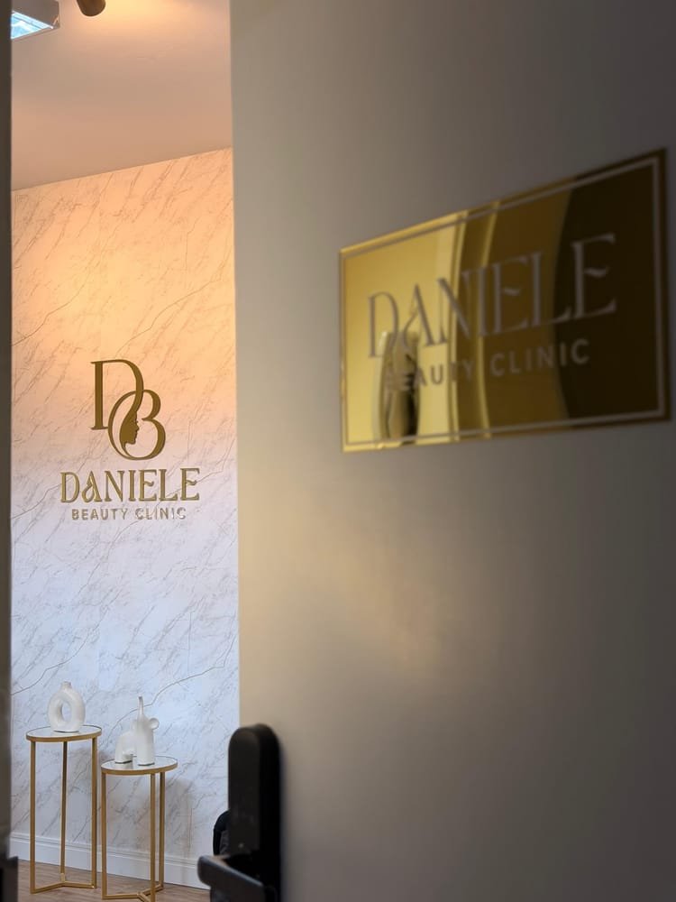 Entrada da clínica com parede de mármore e a marca Daniele Beauty Clinic em dourado